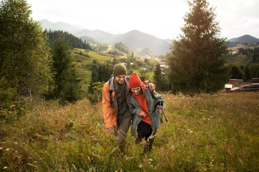 Happy couple walking through a green meadow with views of wooded Black Forest mountains at Maison Talmühle boutique resort