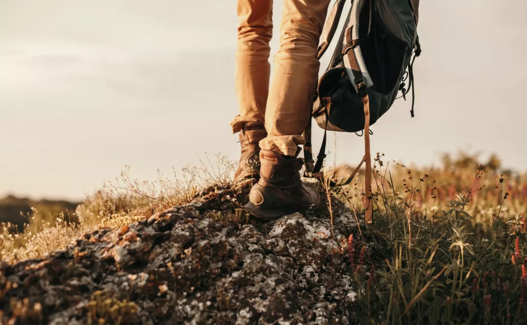 Hiker wearing a backpack and walking boots standing on rocky ground in the countryside at sunset
