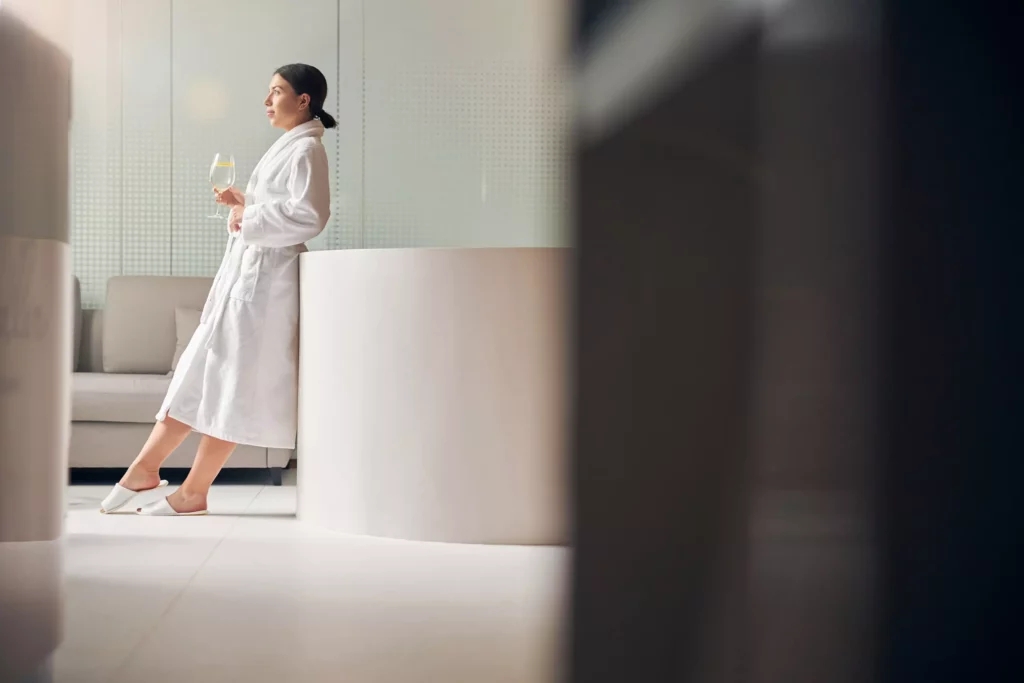 Femme en peignoir blanc tenant un verre d'eau dans un spa boutique du Schwarzwald, ambiance détente et bien-être.