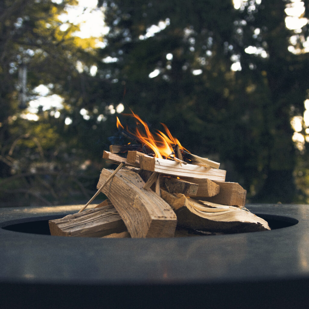 Feuerring mit brennendem Holz vor unscharfem Schwarzwald-Hintergrund im Maison Talmühle Resort Spa