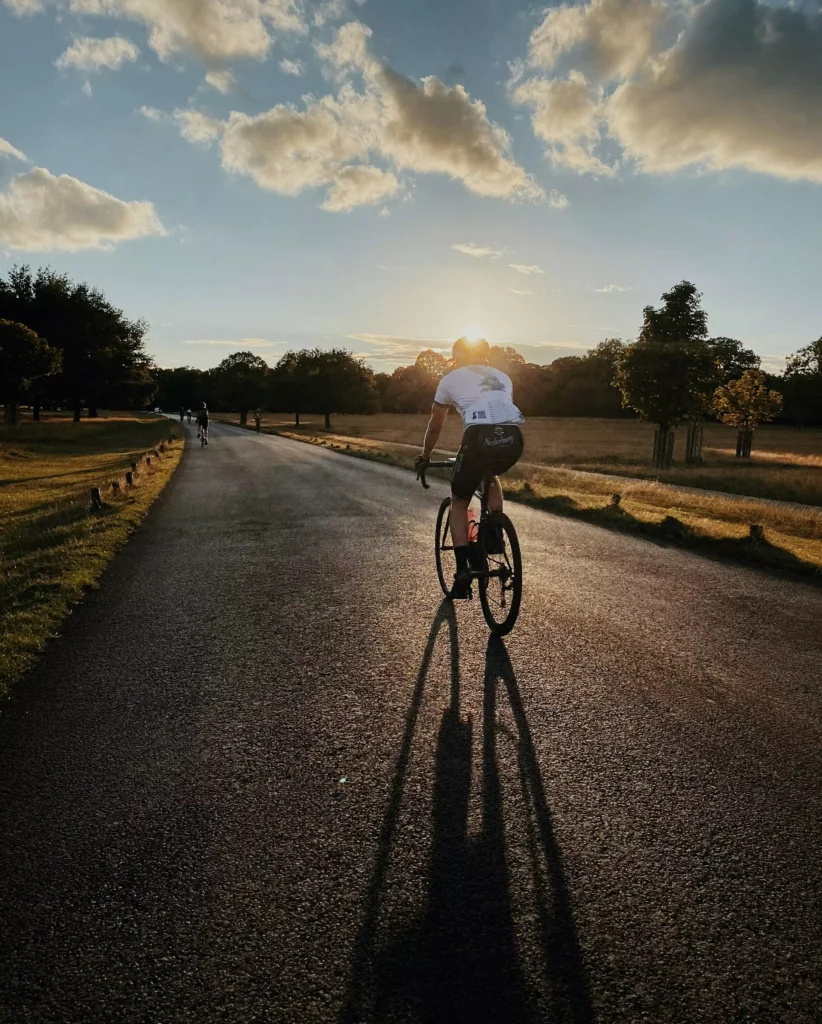 Cyclist on a country road at sunset, with long shadows and trees beside the road in the Black Forest