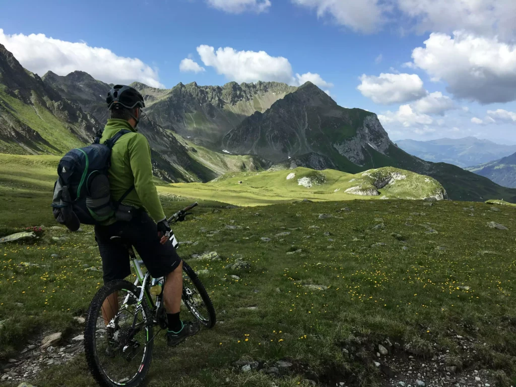 Mountain biker wearing a helmet and backpack looking across a green Alpine landscape with mountains and blue sky at the Black Forest resort