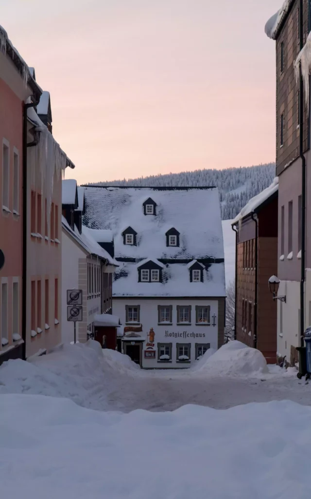 Wintry village street in the Black Forest with snow-covered houses and icicles hanging from roofs at dusk