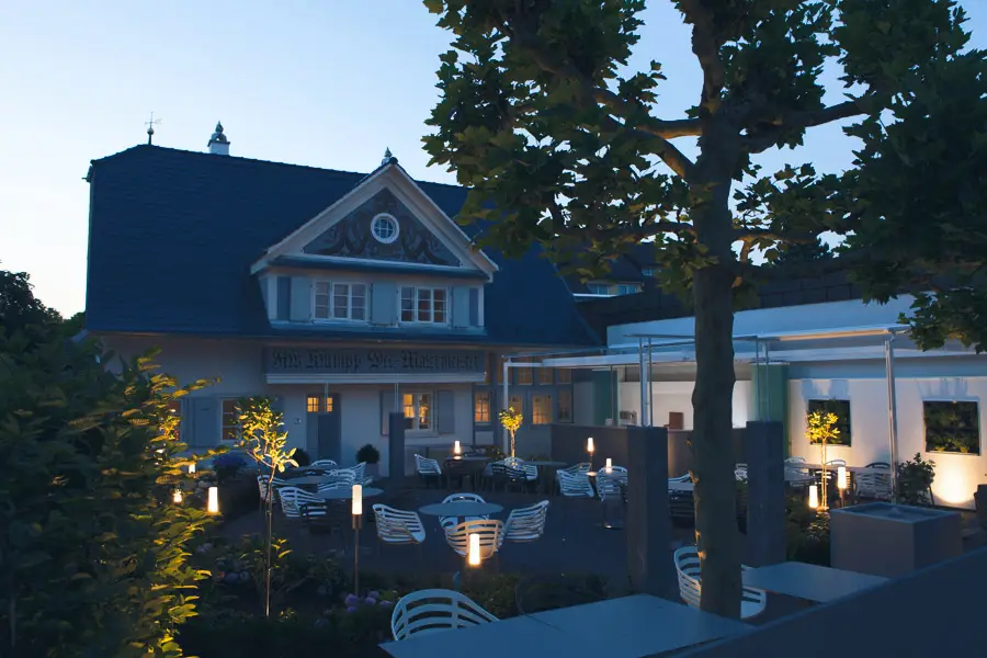 Abendliche Außenansicht des Maison Talmühle Malerhaus mit beleuchtetem Sitzbereich und Bäumen im Schwarzwald Resort
